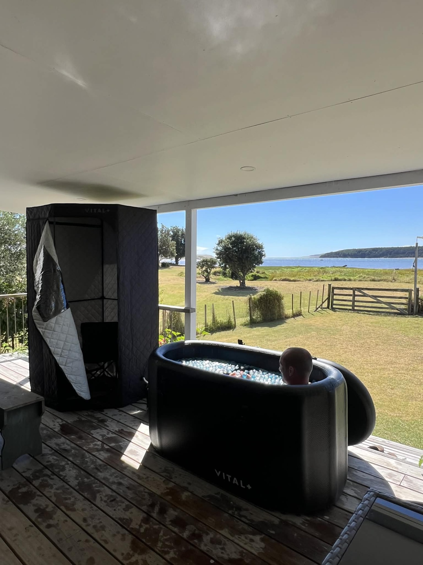 A sauna tent and ice bath side by side on a covered deck with a sea view